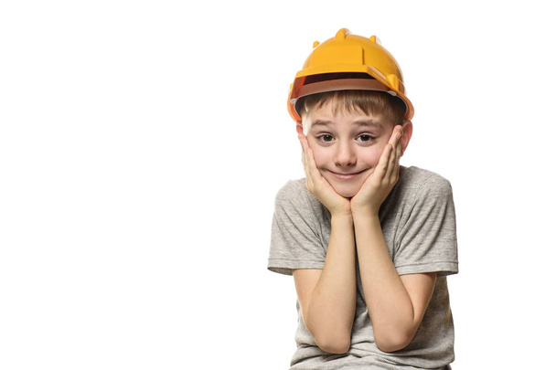 Мальчик в оранжевом строительном шлеме положил руки на щеку. Портрет. Изолировать на белом фоне
. - Фото, изображение