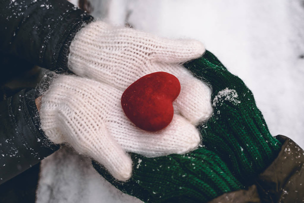 Hands in gloves holding heart closeup on winter snow background. Toned. - Foto, imagen