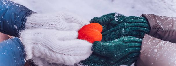 Hands in gloves holding heart closeup on winter snow background. Toned. - 写真・画像