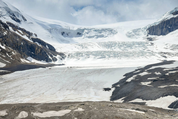 COLUMBIA ICEFIELD, ALBERTA, CANADA - ΙΟΥΝΙΟΣ 2018: Ο παγετώνας Athabasca στο Columbia Icefield στην Αλμπέρτα του Καναδά. Η κλίμακα φαίνεται στη μέση αριστερά από τα φορτηγά και τους ανθρώπους στον παγετώνα. - Φωτογραφία, εικόνα