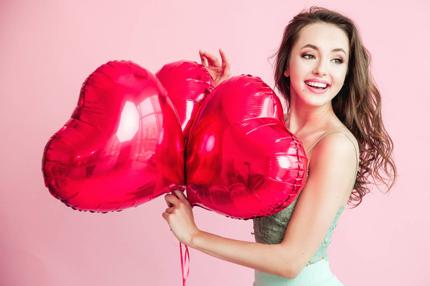 Happy young woman with red balloons smilling over pink background. - Foto, immagini