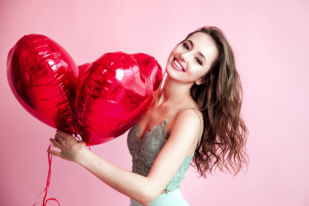 Happy young woman with red balloons smilling over pink background. - Foto, Imagen