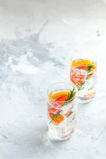 Alcoholic cocktail with grapefruit, soda, ice, gin and rosemary, light gray concrete table background, selective focus, shallow depth of the field. - Fotografie, Obrázek