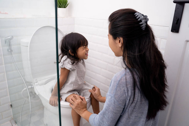 mother help her daughter to sit on the toilet - Foto, Imagen