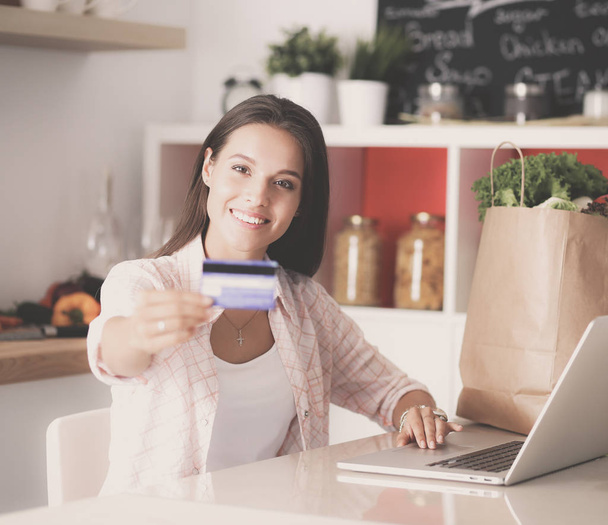 Femme souriante achats en ligne en utilisant tablette et carte de crédit dans la cuisine
 - Photo, image