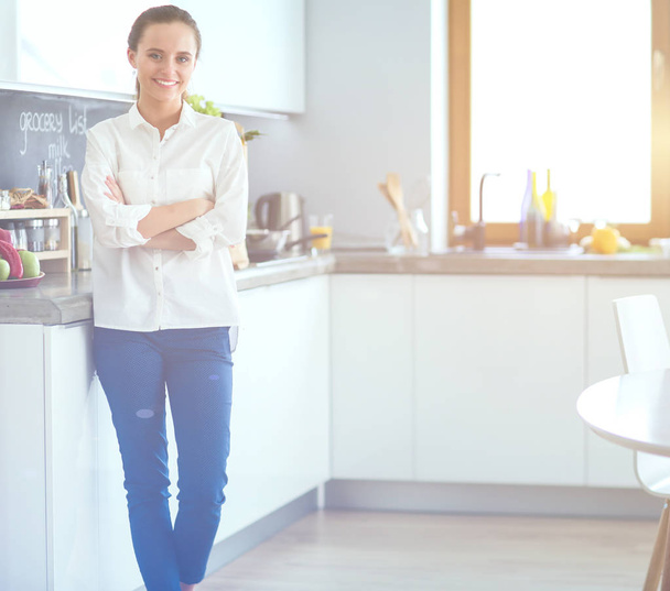 Portrait of young woman standing with arms crossed against kitchen background. Woman in the kitchen. - Foto, afbeelding