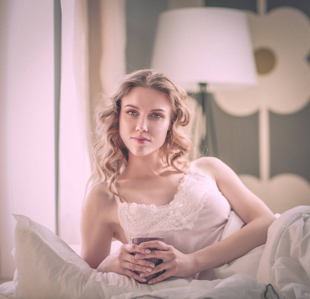 Young woman drinking cup of coffee or tea while lying in bed. - Φωτογραφία, εικόνα