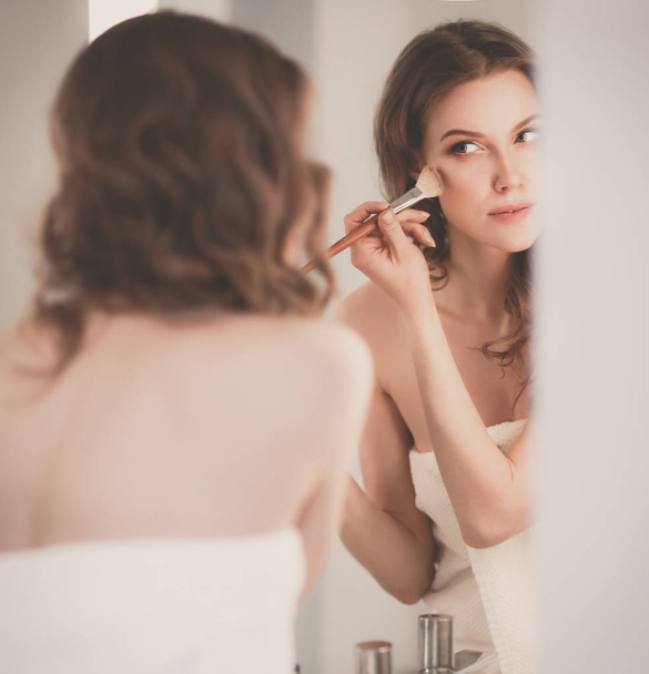 Young woman looking in the mirror and putting make-up on. - Zdjęcie, obraz
