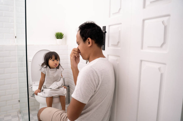 father close his nose when accompanying his daughter to defecate - Fotoğraf, Görsel