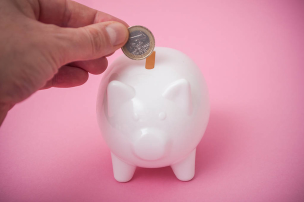 closeup των χεριών του ανθρώπου βάζοντας κέρμα του ευρώ σε λευκό κουμπαράς σε ροζ φόντο - Φωτογραφία, εικόνα