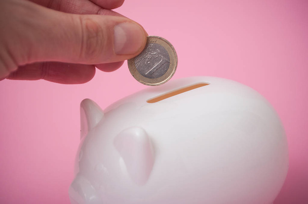 ピンク色の背景に白の貯金箱でユーロ硬貨を入れて男の手のクローズ アップ - 写真・画像