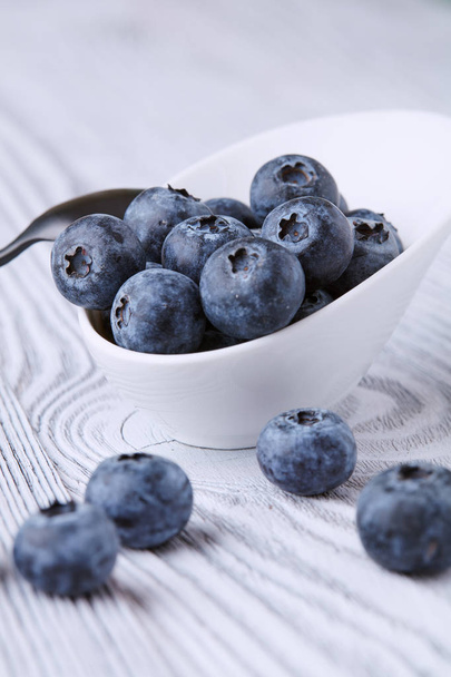 Ripe and sweet blueberries on a textured wooden table in a beautiful white ceramic Cup - Fotografie, Obrázek