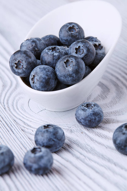 Ripe and sweet blueberries on a textured wooden table in a beautiful white ceramic Cup - Foto, Bild