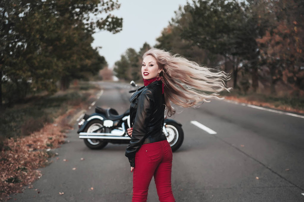 Uma mulher motociclista elegante posando com uma motocicleta na estrada
. - Foto, Imagem