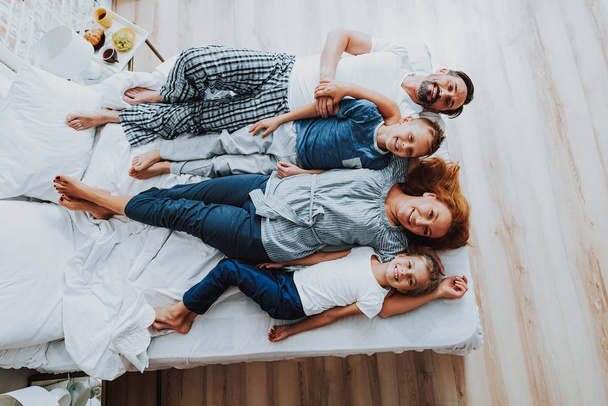 Joyful parents with their kids laying on bed - Фото, изображение