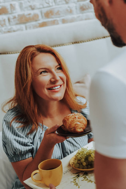 Happy smiling woman holding croissant on plate - Fotó, kép