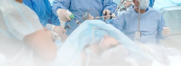 Blur.A ομάδα χειρουργών χρησιμοποιώντας ενδο-όργανα λειτουργούν κοιλιά του ασθενούς. Χειρουργική επέμβαση στο σώμα του μια πλήρη γυναίκα. Endovideosurgery.Operating δωμάτιο στο νοσοκομείο. Χειρουργικό τραπέζι. Πανόραμα. Ενδοσκόπηση. - Φωτογραφία, εικόνα