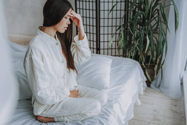 Unhappy asian woman in pajamas feeling sick on soft bed - Foto, Bild