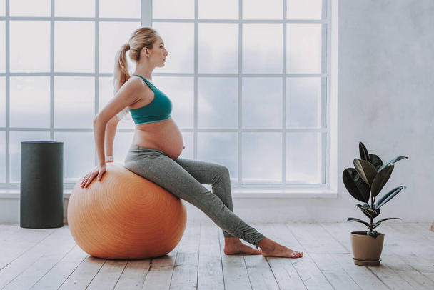 Active pregnant woman doing pilates exercises in cozy living room - Foto, afbeelding