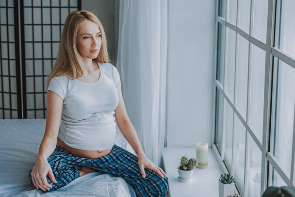Calm pregnant woman looking out of window in light bedroom - Photo, Image