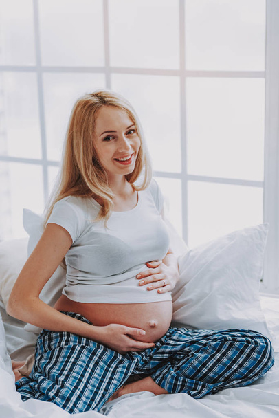 Smiling pregnant woman is posing at camera - 写真・画像