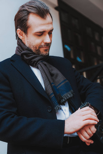 Trendy businessman in black coat is checking time - Foto, afbeelding