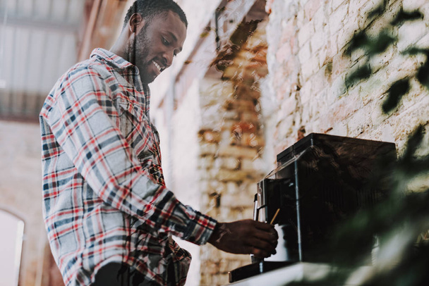 Waist up of positive Afro-American man using coffee machine and smiling - Valokuva, kuva