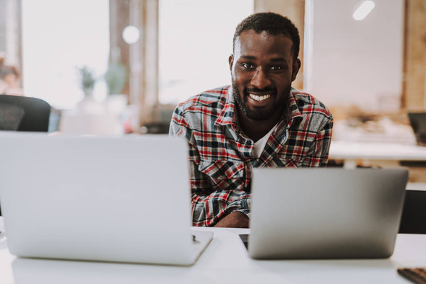 Positive Afro-American man smiling and using two modern laptops - Valokuva, kuva