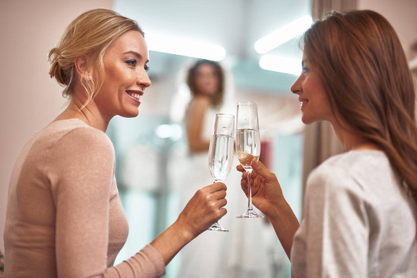 Smiling ladies sitting in showroom with champagne - Foto, imagen