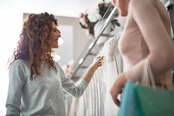 Cheerful lady choosing bridal dress in wedding shop - Foto, afbeelding