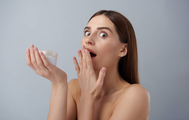 Astonished young lady with cosmetic product covering wide open mouth with hand - Foto, Bild