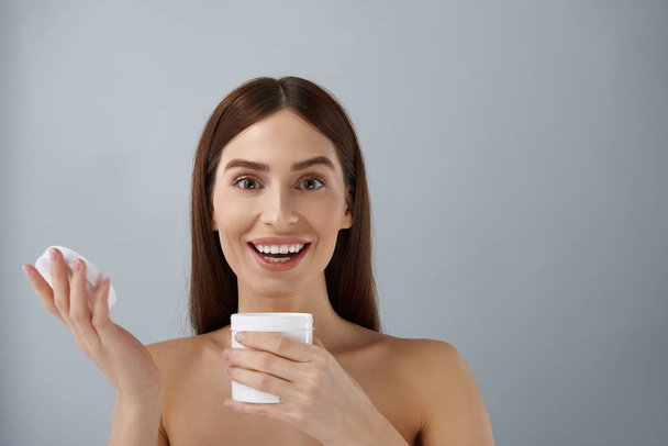 Happy young lady holding opened jar of cosmetic cream - Фото, изображение