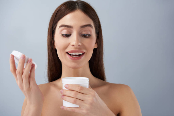 Cheerful young lady opening white jar of cosmetic cream - Foto, Imagen