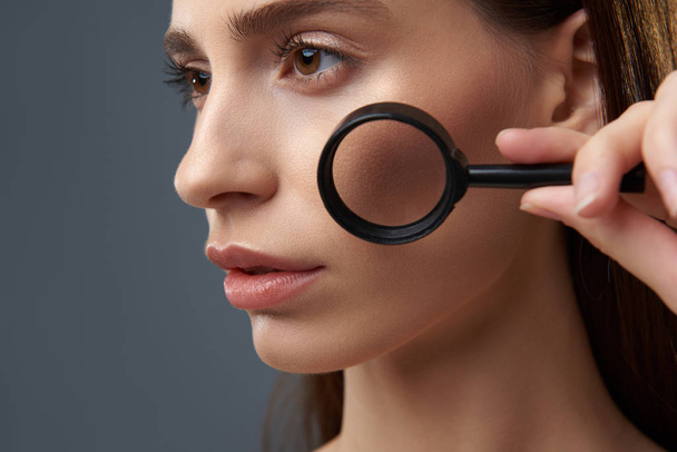 Beautiful young woman with perfect skin using magnifying glass - Foto, Bild