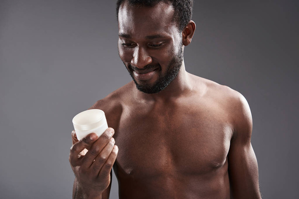 Cheerful handsome afro America man holding a cream jar - Фото, зображення