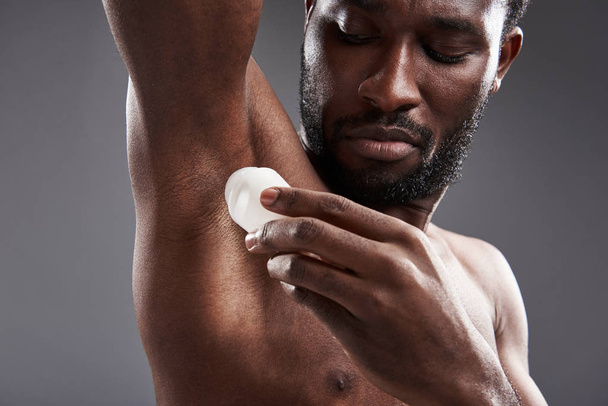 Serious afro American man applying deodorant on the armpits - Foto, afbeelding