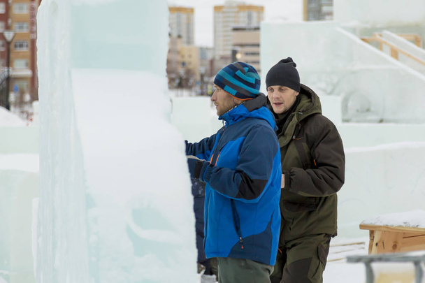 Um trabalhador se aproxima de um artista que desenha em um bloco de gelo
. - Foto, Imagem