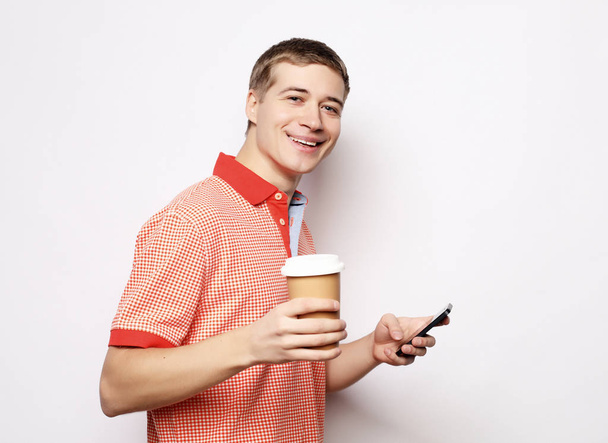 young man  talking on mobile phone, drinking takeaway coffee - Фото, изображение
