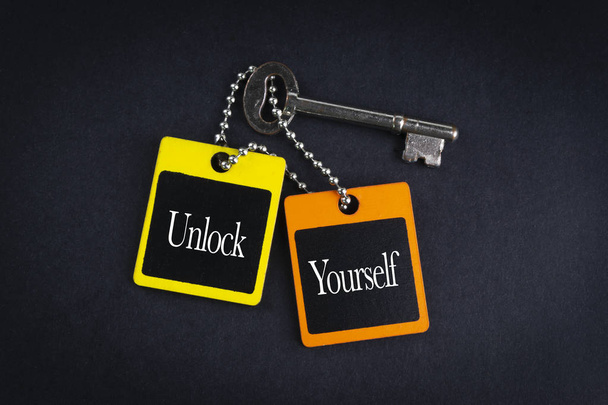 UNLOCK YOURSELF inscription written on wooden tag and key on black background with selective focus and crop fragment. Business and education concept - Photo, Image