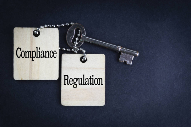 COMPLIANCE REGULATION inscription written on wooden tag and key on black background with selective focus and crop fragment. Business and education concept - Photo, Image