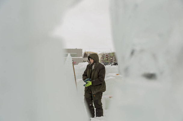 Ritratto di un operaio in giacca verde con cappuccio impegnato nella sistemazione di una città di ghiaccio
 - Foto, immagini
