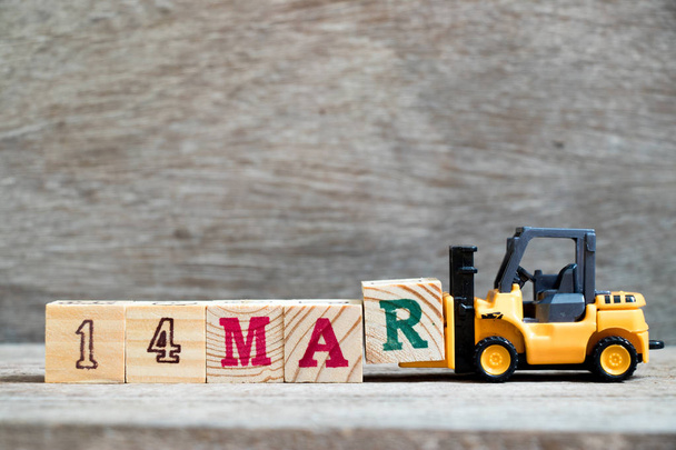 Toy forklift hold block R to complete word 14mar on wood background (Concept for calendar date 14 in month March) - Photo, Image