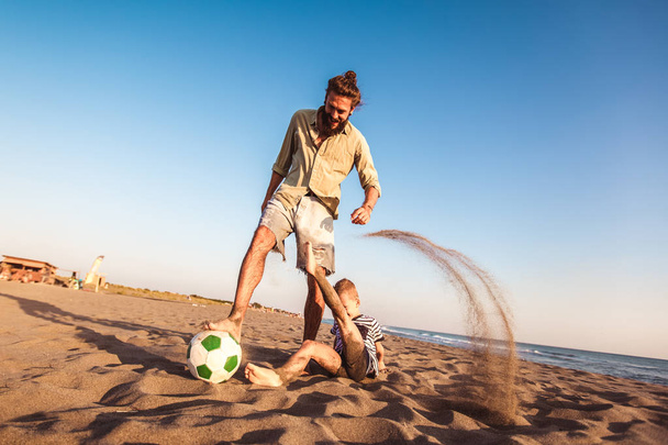 glücklicher Vater und Sohn spielen Fußball oder Fußball am Strand und genießen die Zeit mit der Familie im Sommerurlaub. - Foto, Bild