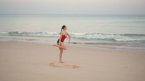 Nő a piros smiwsuit gyakorló jóga fitness gyakorolja a strandon napkelte előtt - Felvétel, videó
