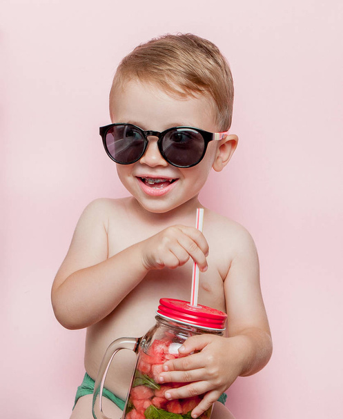 Little boy with Jar of cold fresh lemonade with piece of watermelon and ice on pink background. - Fotografie, Obrázek