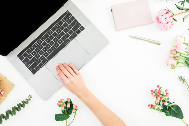 Woman typing on laptop. Workspace with female hands, laptop, notebook and pink flowers on white background. Top view. Flat lay. - Photo, Image