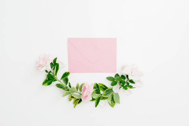 Цветочный состав бумажного конверта с розовыми розами и зелеными листьями на белом фоне. Плоский, вид сверху
 - Фото, изображение
