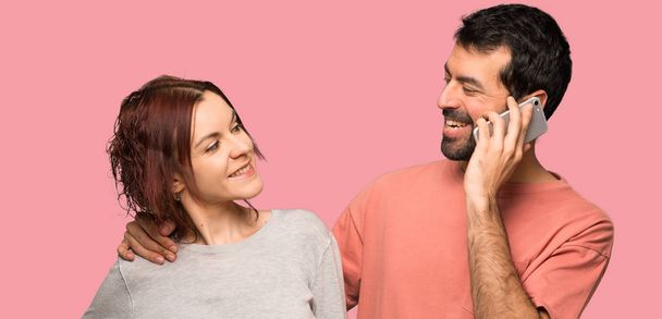 Couple in valentine day keeping a conversation with the mobile phone over isolated pink background - Photo, image