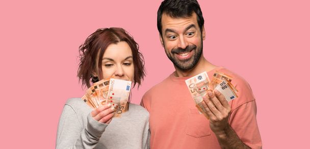 Couple in valentine day taking a lot of money over isolated pink background - Фото, изображение