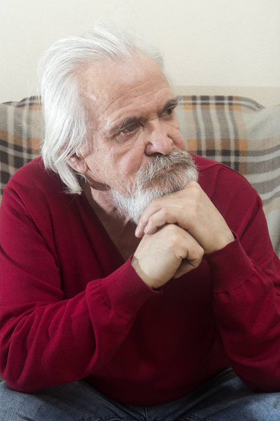 A handsome sick old man with a beard and a mustache with long white hair in a nursing home sits in an armchair all alone and reflects on the past years - Photo, Image